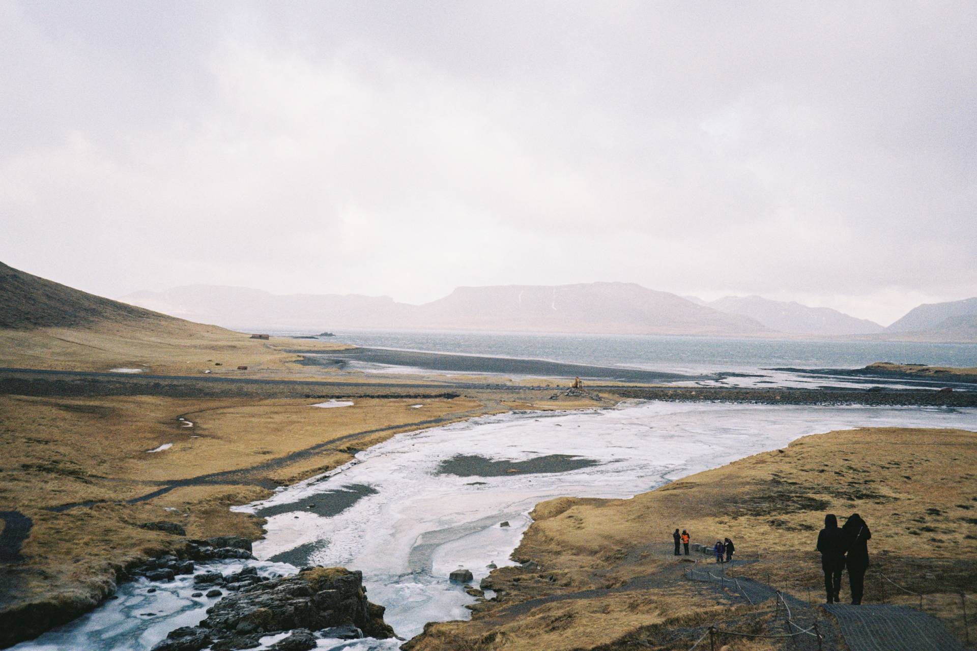 A photograph of a barren landscape with a glacier river running into a lake