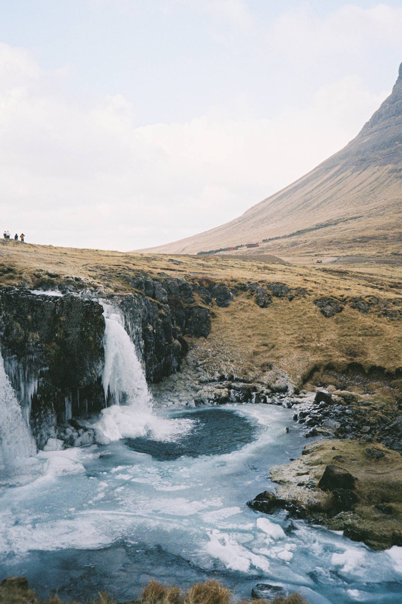 A photograph of an icy waterfall with a sharp hill in the background