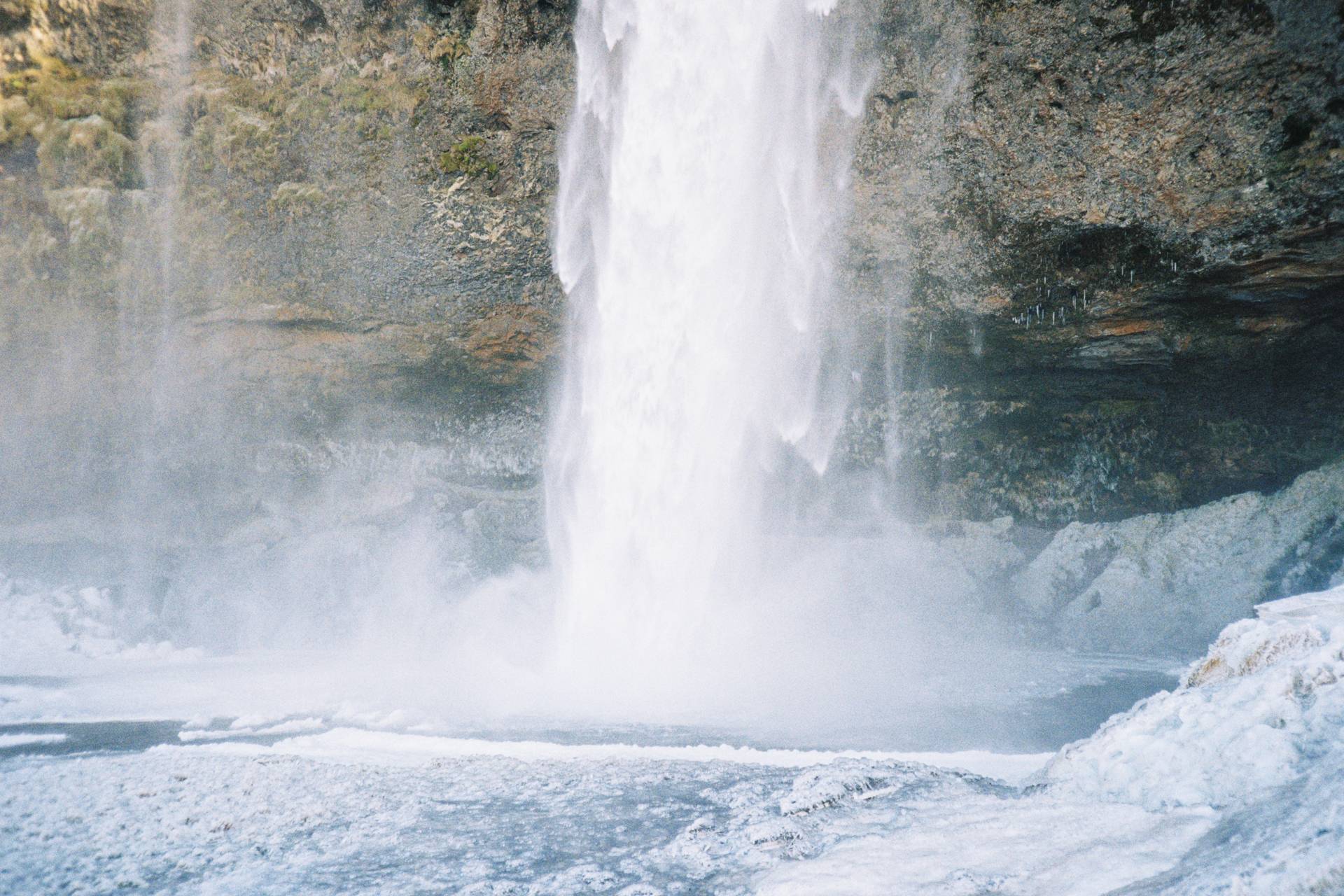 A photograph of the bottom of an icy waterfall hitting the ground