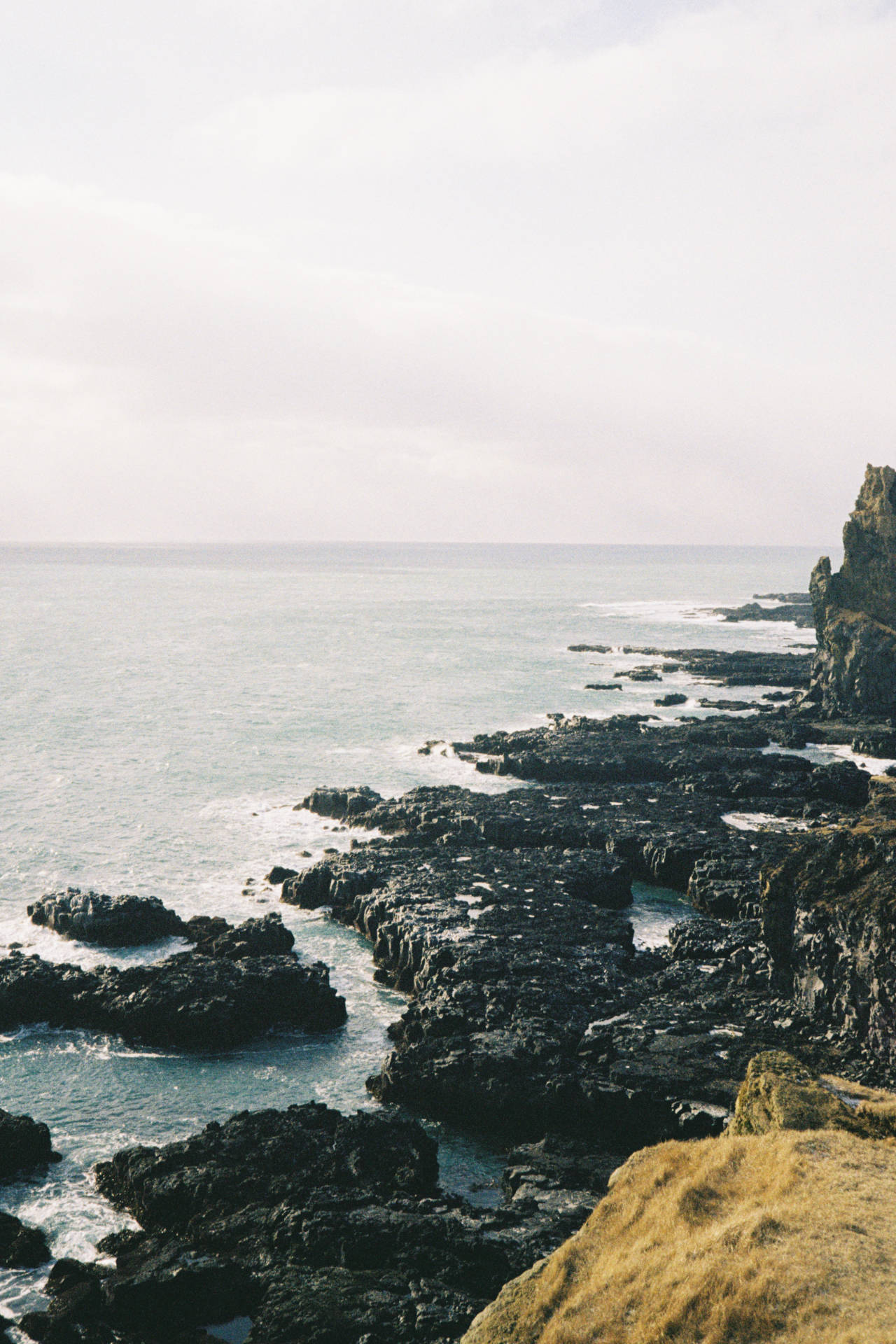 A photograph of some black rocks off the side of a cliff by the sea